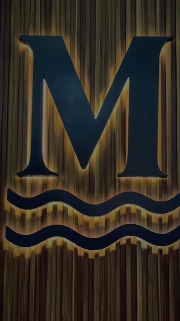 La M y las olas de Mareva iluminadas sobre una pared de madera del restaurante